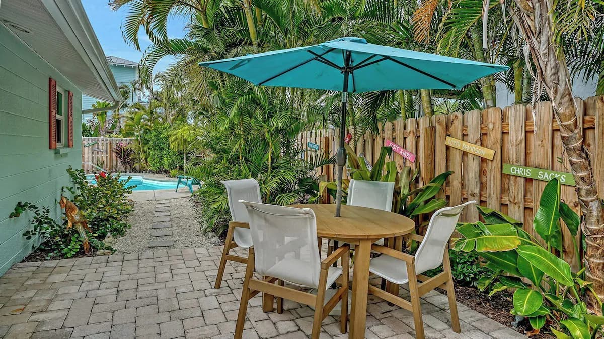 Round wooden table and white chairs under a turquoise umbrella on the cottage's patio